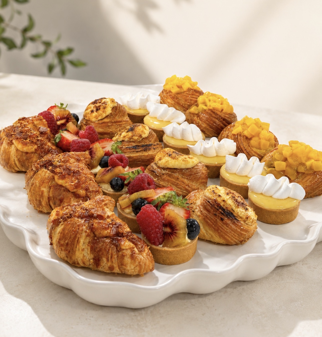 A platter of mini croissants, lemon tartlets and fruit tarts for events